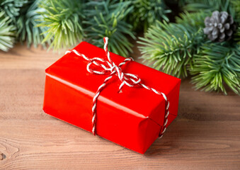 Christmas postcard gift box in red paper with fir branches on a wooden background.