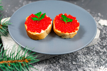 Sandwiches with red caviar on a gray plate on a table with branches of a Christmas tree. Christmas, New Years holidays. Festive food.