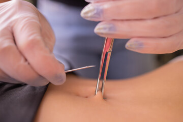 The first piercing. Dressing the earrings on the navel. Female piercing.