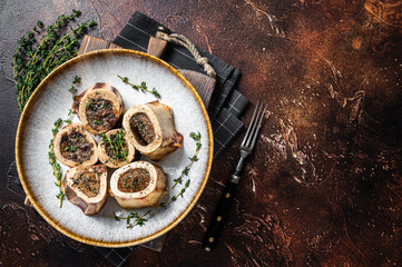 Baked marrow veal beef bones in plate with thyme and herbs. Dark background. Top view. Copy space