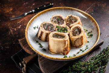 Baked marrow veal beef bones in plate with thyme and herbs. Dark background. Top view