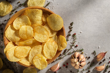 Chips, potato crisps heap with garlic, rosemary, in bowl on grey stone background. Junk food or...