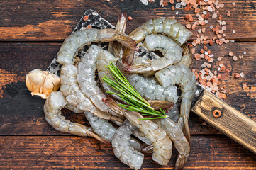 Raw Headless tiger shrimps prawns on a butcher cleaver. Dark wooden background. Top view - obrazy, fototapety, plakaty