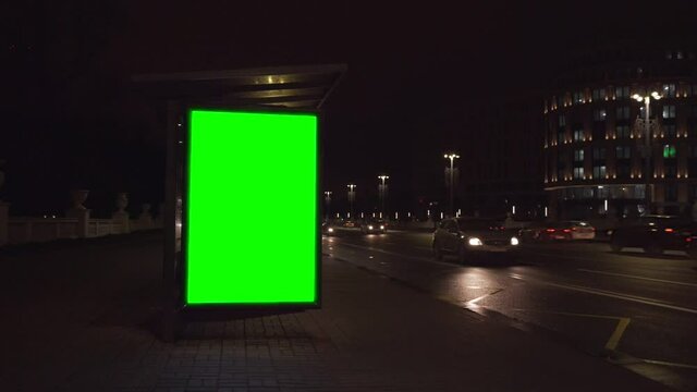 Blank vertically lightbox with green chroma key place for mockup on city street at night with vehicle traffic. Concept commercial public information and advertising marketing.