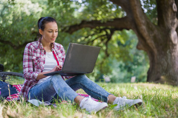 Young woman freelance entrepreneur working on her laptop computer out in the nature. Global wi-i network. Using mobile information devices outdoors