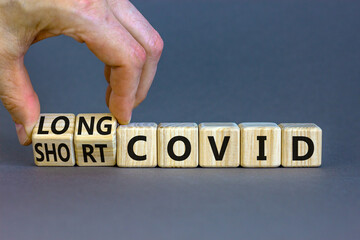 Long covid symbol. Doctor turnes wooden cubes and changes words ' long covid' to 'short covid'. Beautiful grey table, grey background, copy space. Medical, covid-19 pandemic long covid concept.
