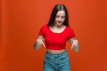 Stylish young girl girl smiling pointing down, recommend product, advertising shopping sales on orange background