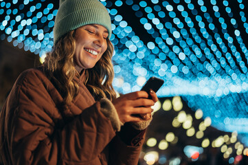 Young woman using a smartphone outside with the decorative christmas lights in the background