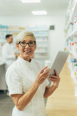 Fototapeta premium Beautiful senior female pharmacist checking medications on a shelf