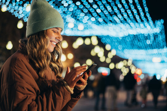 Young woman using a smartphone outside with the decorative christmas lights in the background