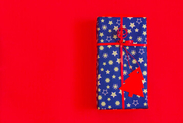 festive gift box in blue in silver stars with red paper christmas tree decoration on red background with copy space