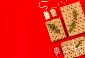 gift boxes wrapped in beige craft paper and spools of rope for packaging on a red background with copy space, top view