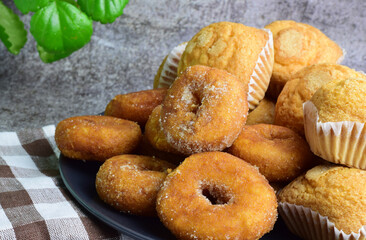 Sugar donuts, muffins on plate, interior, kitchen with green leafy plant. Stone background.