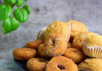 Sugar donuts, muffins on plate, interior, kitchen with green leafy plant. Stone background.