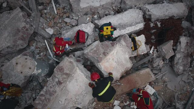 Zoom out drone view of rescuers and paramedics examining concrete debris of demolished building after earthquake