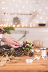 Woman artisan making Christmas holiday wreath on a table among by New Year's decor