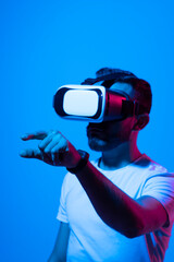 Handsome young man in VR headset is gesturing and try to touch to something that he see. Virtual reality concept.