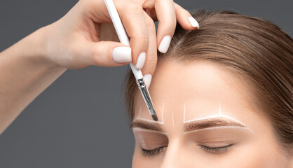 Make-up artist makes markings with white pencil for eyebrow and paints eyebrows. Professional...