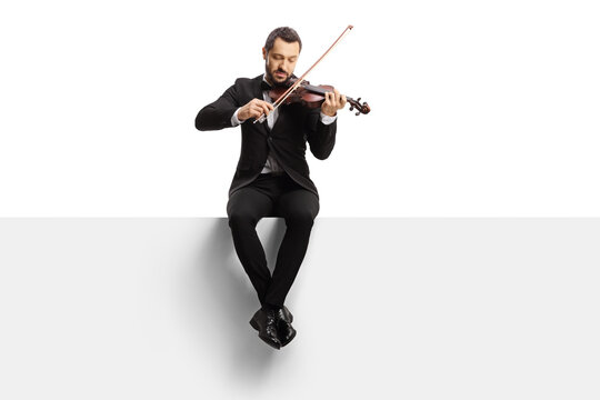 Full length shot of a violinist sitting on a blank panel and playing a violin