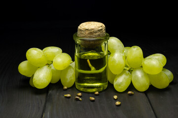 Grape oil seed in small vintage bottle. Heap of grape seeds with green slices and cold press organic essential oil, tincture, extract, infusion on wooden rustic background closeup