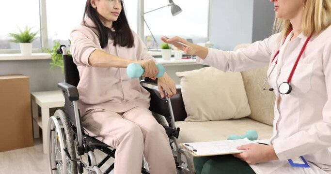 Doctor together with woman in wheelchair is doing physical exercises with dumbbells