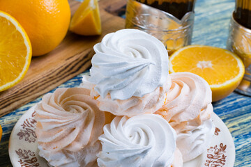 Delicious marshmallow with orange filling in a vintage plate, sliced orange on a cutting board and glasses with black tea