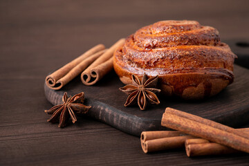 Composition of baked cinnamon bun on dark wooden table. Cinnamon sticks and anise star on wooden background