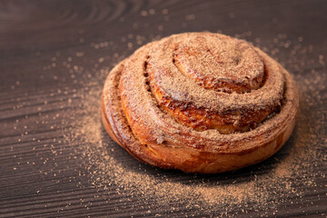 One tasty cinnamon bun on wooden table seasoned with ground cinnamon. Cooking at home