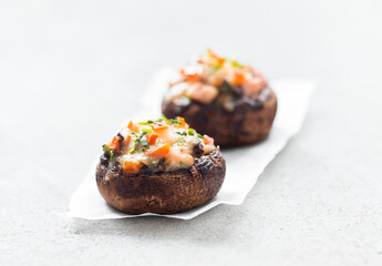 Hot appetizer, Stuffed mushrooms with ham, cheese, tomatoes and parsley on paper on a light gray background