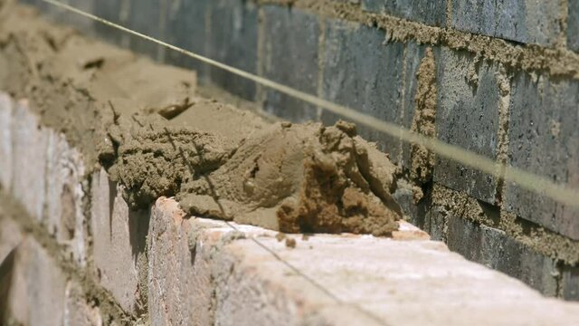 CLOSE UP, Mortar Troweled Onto Row Of Bricks At Housing Construction Site
