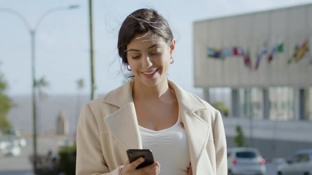 Attractive and Cheerful Young Woman Using Smartphone in Crowded Street. Talking on The Phone While Walking