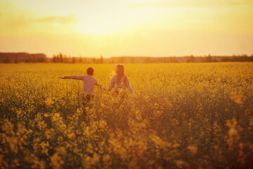 Children run on a rye field. Brother and sister run across the field holding hands. Sunset light in summer field. Image with selective focus, toning and noise.