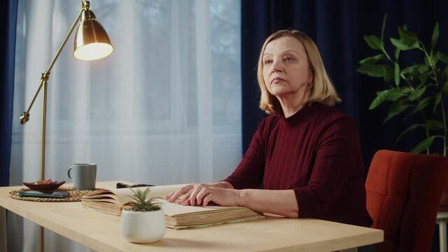 Blind woman reading braille book using fingers, sitting in living room, poorly seeing female person learning to read, home education for people with disabilities, touching letters on sheet of paper.