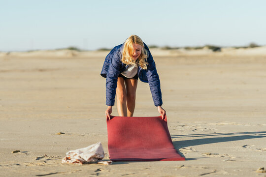 Female Rolling Out A Yoga Mat On The Beach