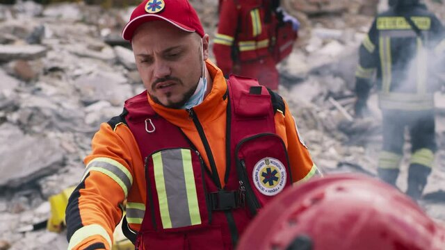 Bearded man in paramedic uniform pointing away and giving instructions to coworker during rescue mission after disaster