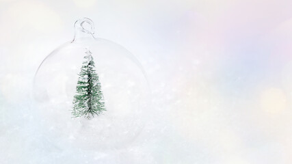 Shiny, glass Christmas ball with a miniature Christmas tree on the snow on a light background.