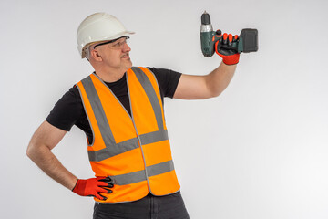Builder with Power Screwdrivers. Man examines Power Screwdrivers. Power Tools concept for professional builders. Man holds Screw Guns. Man in orange vest. Repair specialist on light background