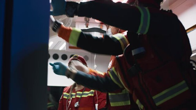 Low angle of medical practitioners in uniform and masks preparing equipment in hurry while taking care of patient in ambulance car during emergency at night