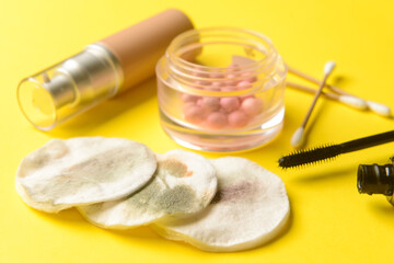 Used cotton pads, mascara, cotton buds, blushes and mascara on yellow table, closeup