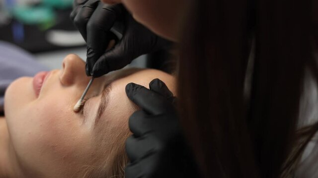 Woman doing eyelashes lamination in beauty studio. Blond hair model has staining, curling, laminating and extension for lashes. Close-up