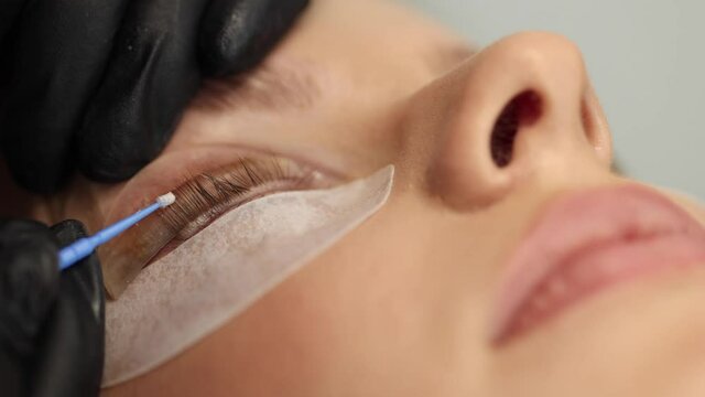 Close-up of eyelash care treatment procedures. Beautiful female, blond hair model have eyelashes lamination. Woman doing staining, curling, laminating and extension for lashes. Macro video