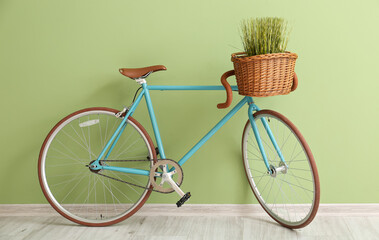 Stylish bicycle with wicker basket and grass near green wall