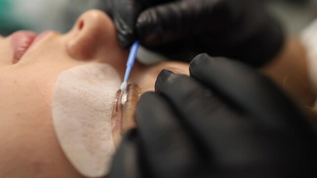 Close-up of eyelash care treatment procedures. Beautiful female, blond hair model have eyelashes lamination. Woman doing staining, curling, laminating and extension for lashes. Side view