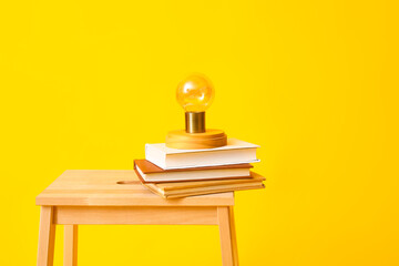 Wooden step stool with books and lamp on yellow background