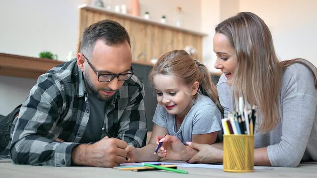 Happy mother, father and daughter drawing picture together use multicolored pencil and paper sheet 
