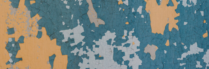Peeling paint on the wall. Panorama of a concrete wall with old cracked flaking paint. Weathered rough painted surface with patterns of cracks and peeling. Wide panoramic grungy texture for background