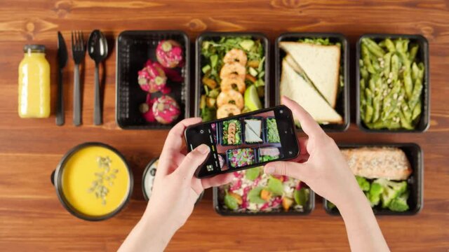 Food delivery top view, take away meals in disposable containers on wooden table. Taking photo of lunch boxes with cooked vegetarian dishes on smartphone. Healthy diet. Catering service concept. 