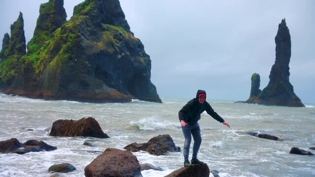 Tourist Stands At The Small Rock At Reynisfjara Beach In Iceland With The Reynisdrangar At The Background. wide shot