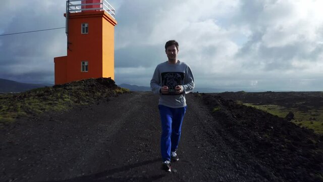 Man With Drone Remote Control Walking On Trail Near Hopsnesviti Lighthouse On Southwest Coast Of Iceland. pullback shot