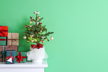Small Christmas tree with gifts on mantelpiece near green wall